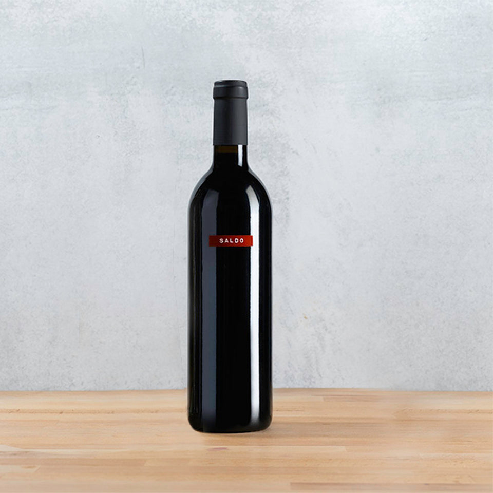 Bottle of SALDO Zinfandel wine on a wooden table against a white wall