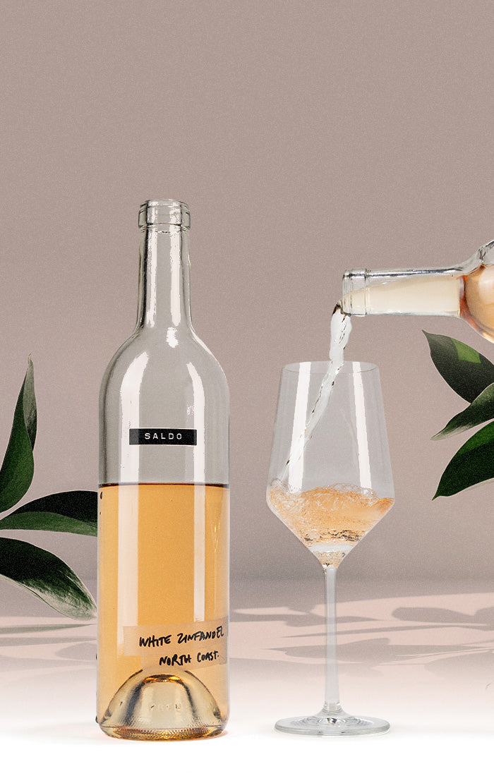 A bottle of Saldo White Zinfandel rests on a table, while another bottle pours into a glass