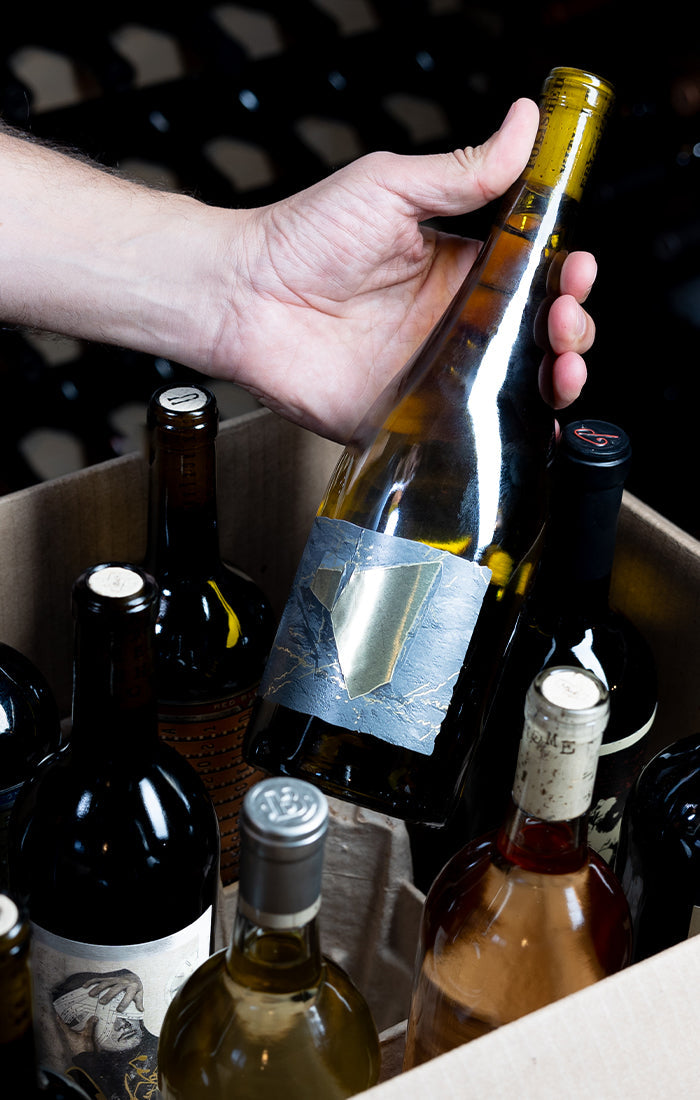 Hand holding a wine bottle with a blurred background of other wine bottles.