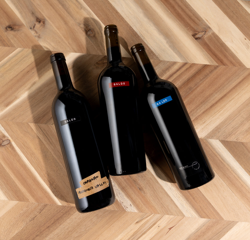 SALDO Red Trio bottles of wine laying down with wooden background