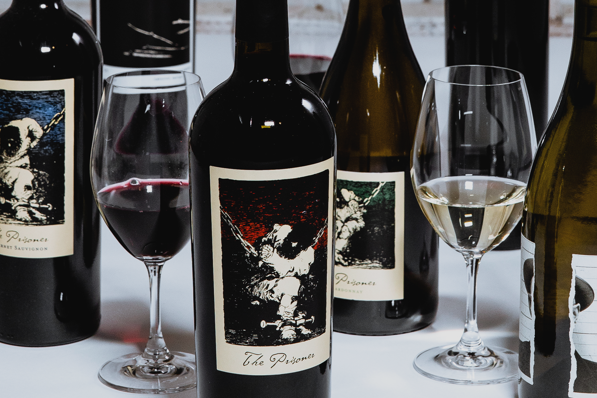 Bottles of The Prisoner Wine Company wine and glasses of wine on white table