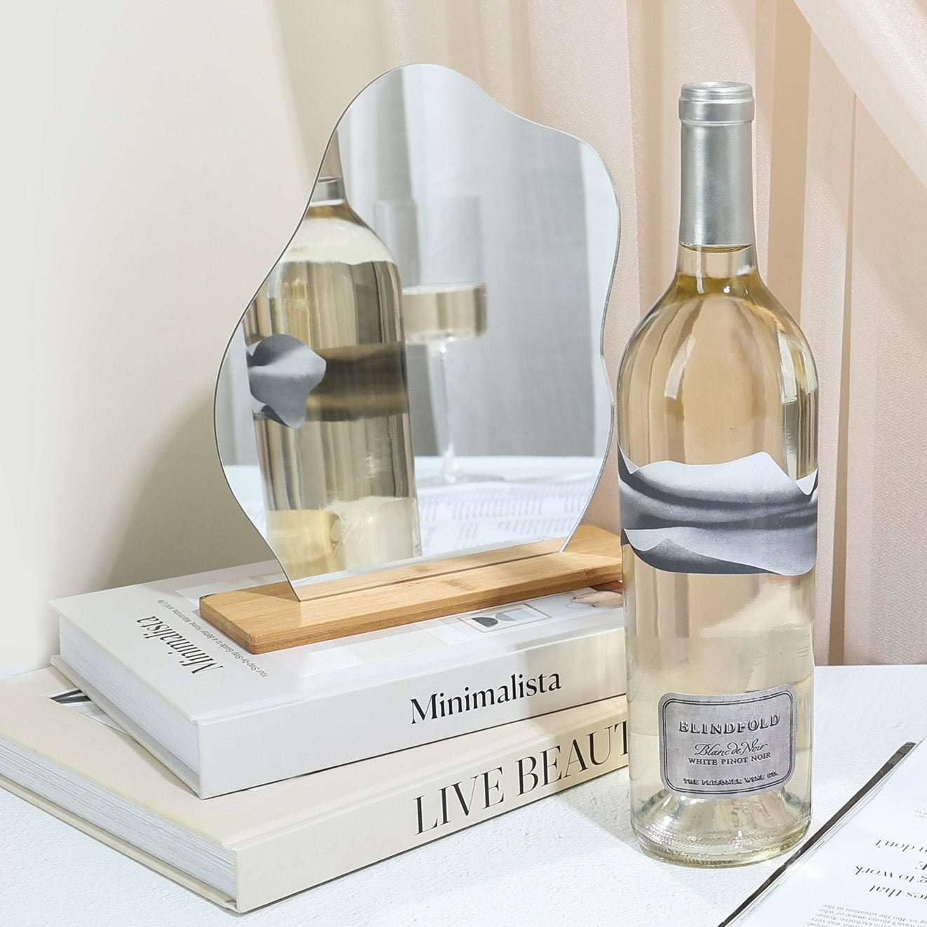Bottle of white wine on a table with decorative items including a mirror, books, and a vase.