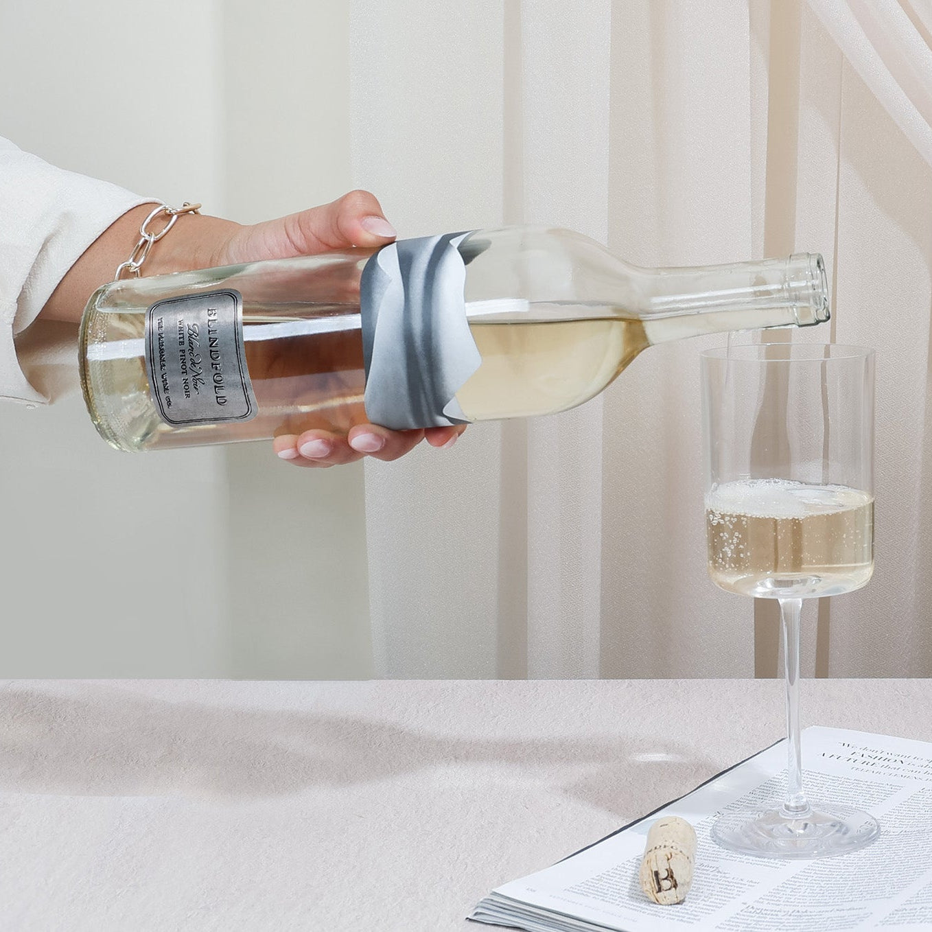 Person pouring wine into a glass on a table with books and decor.
