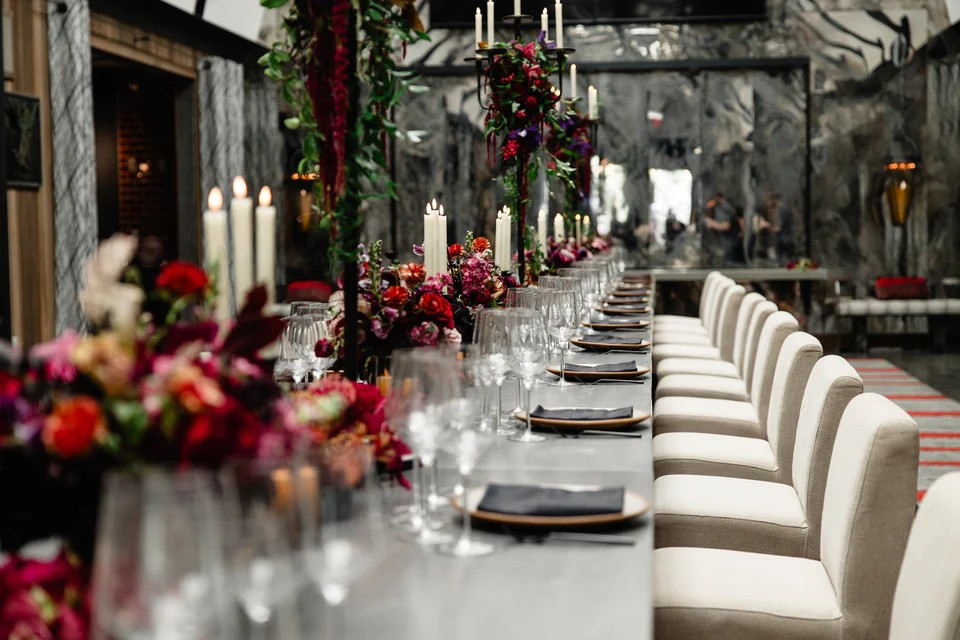 Long dining table set for a formal event with floral arrangements and candles in a stylishly decorated room.