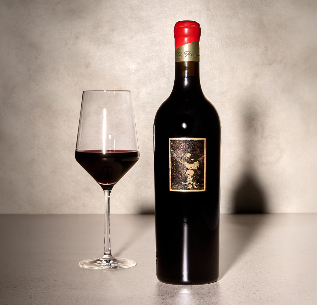 Bottle and glass of red wine on a textured surface with a neutral background