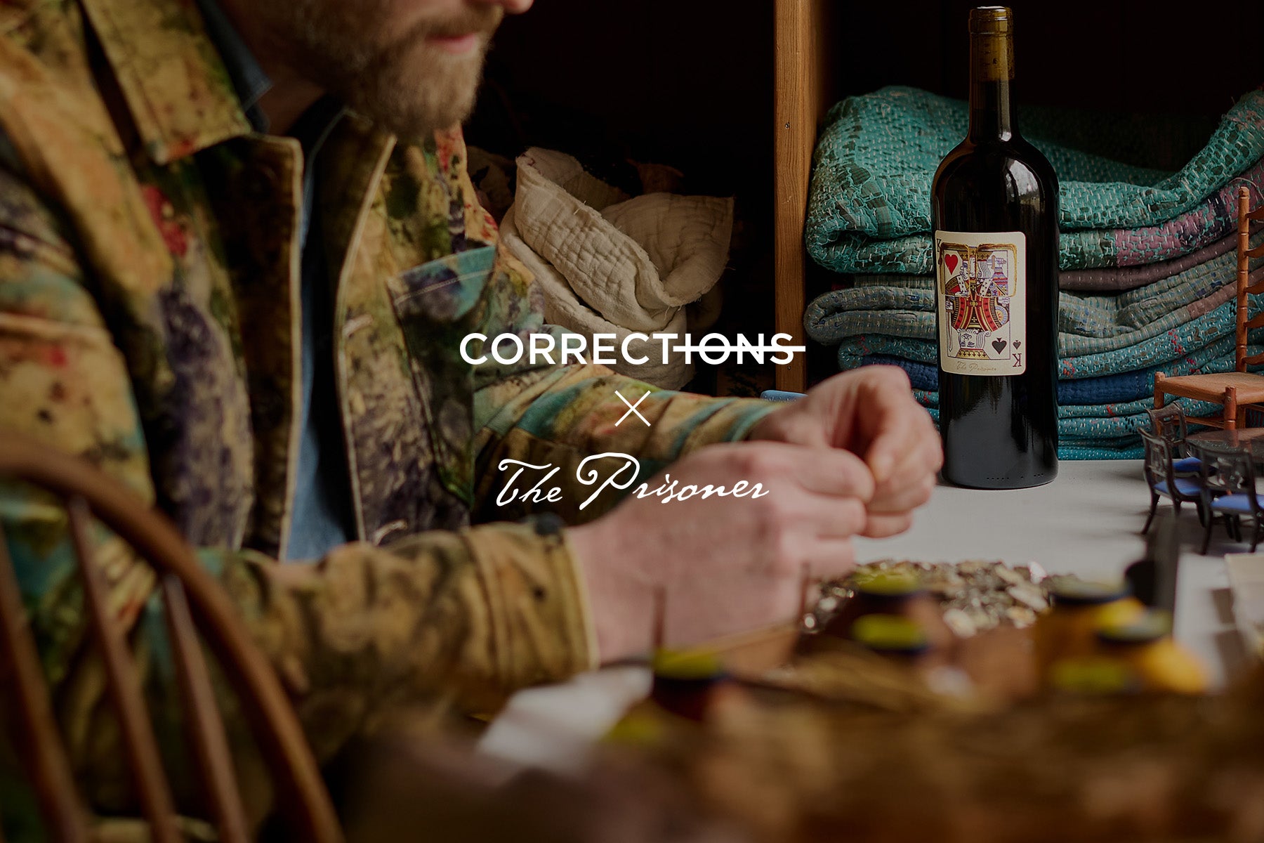 Man sitting at a table with a bottle of wine, surrounded by cozy decor. Title says "Corrections x The Prisoner" 