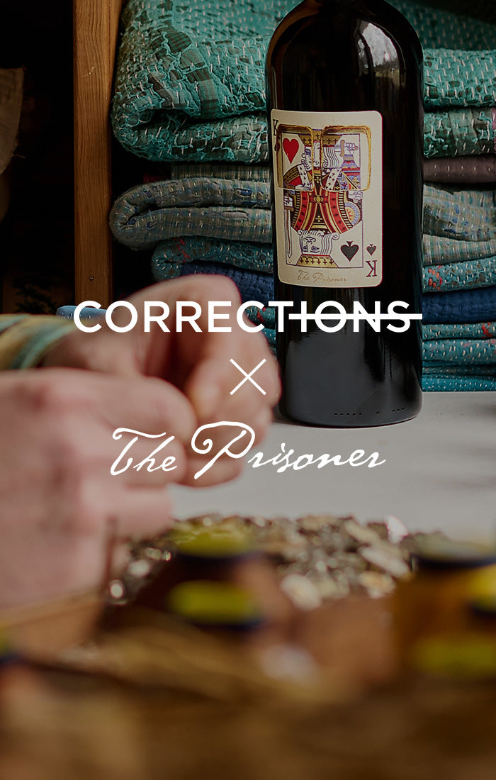 Man sitting at a table with a bottle of wine, surrounded by cozy decor. Title says "Corrections x The Prisoner" 