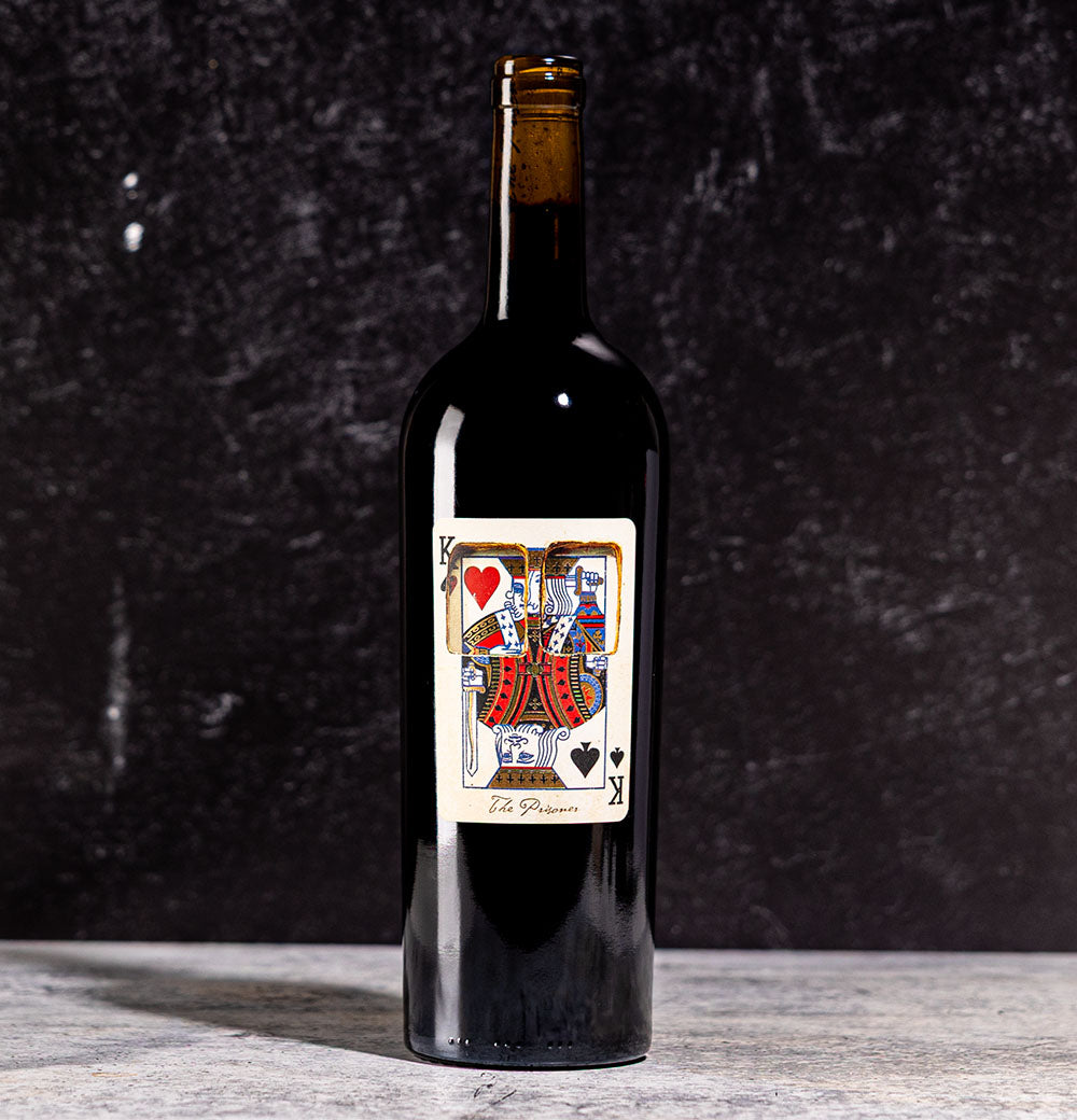 A bottle of The Prisoner x Corrections wine with a playing card label on a dark background