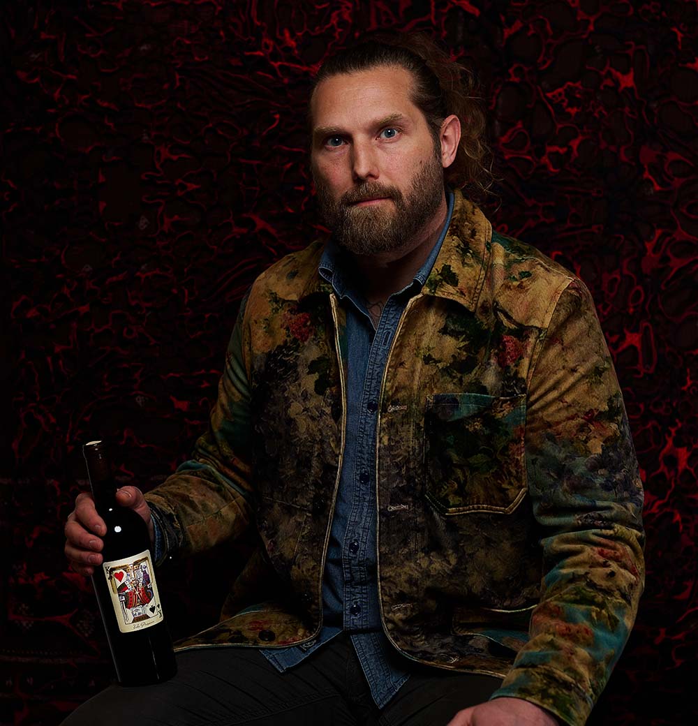 Man holding a bottle of The Prisoner x Corrections wine with a playing card label