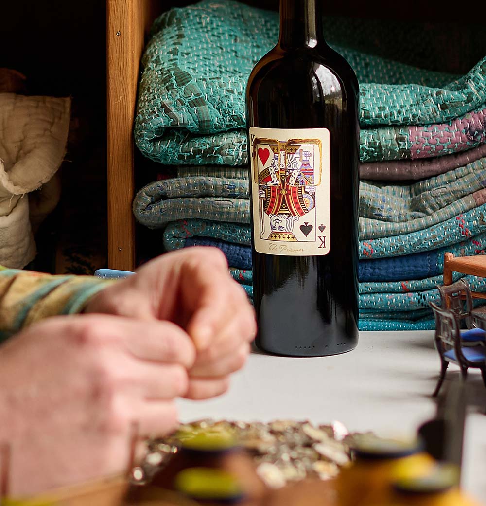 A bottle of The Prisoner x Corrections wine with a playing card label rests on a table