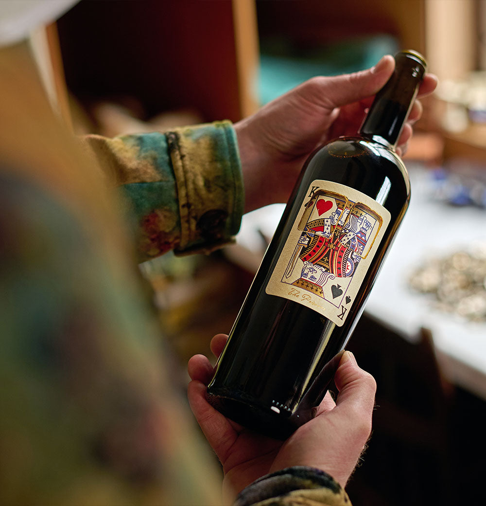 Man holds a bottle of The Prisoner x Corrections wine with a playing card label 