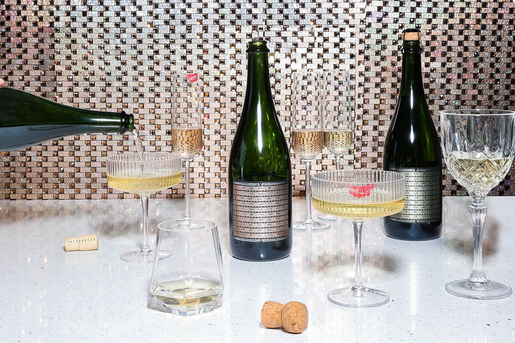 Bottles of Unshackled Sparkling wine next to glasses of wine and corks