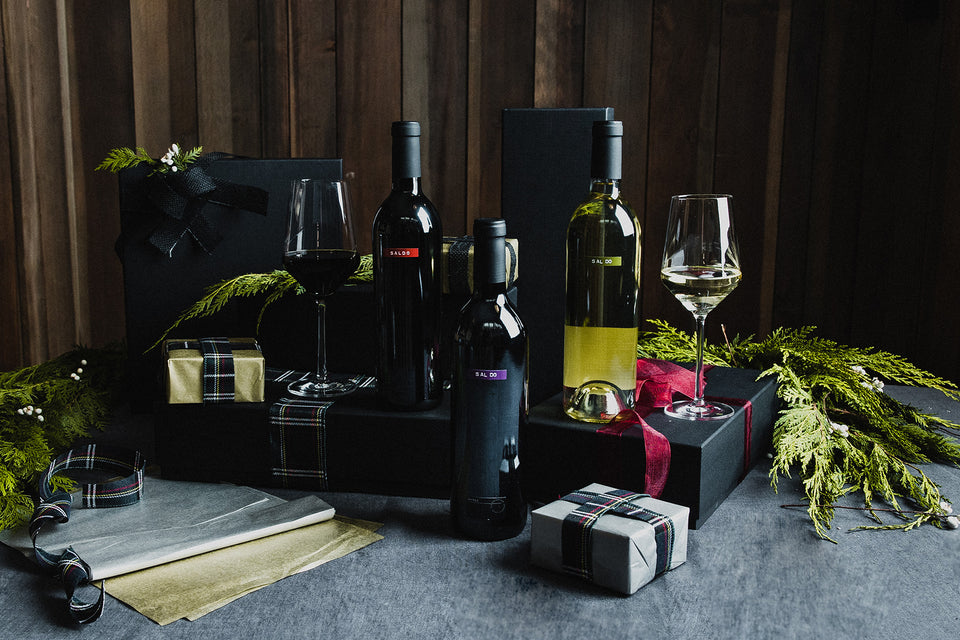 Bottles of SALDO wines on a table with glasses of wine and wrapping paper
