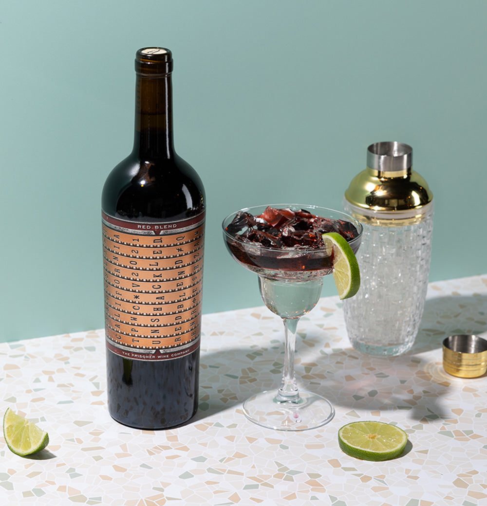 A bottle of Unshackled red blend on a table next to a shaker with a cocktail 