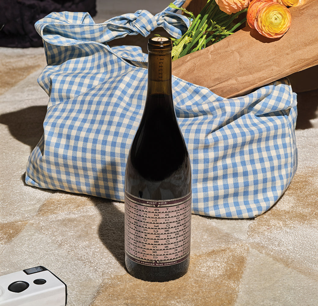 Unshackled Pinot Noir bottle on a checkered blanket with flowers in the background