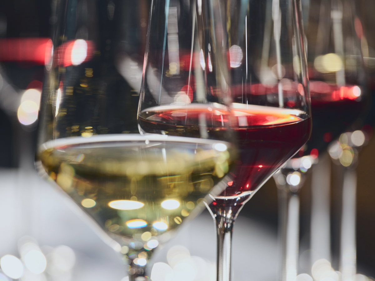 Close-up of several wine glasses, including one filled with white wine and another with red wine, set against a softly blurred background with warm lights.