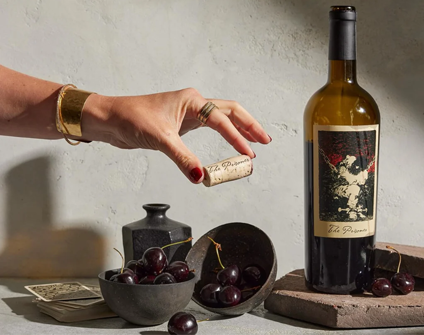 A Bottle of The Prisoner with cherries and a person holding a cork.