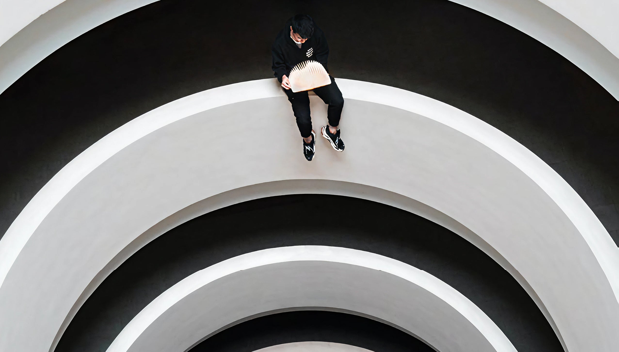 Person sitting on a circular staircase with white walls and black steps